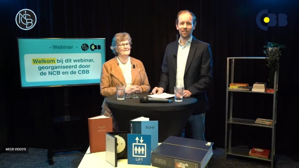 Links op de afbeelding is een tv-scherm te zien, met daarop tekst. Rechts daarvan staan twee personen aan een statafel. Voor hen staat lectuur in diverse leesvormen. Rechts in beeld staat een kast met een paar voorwerpen erin.